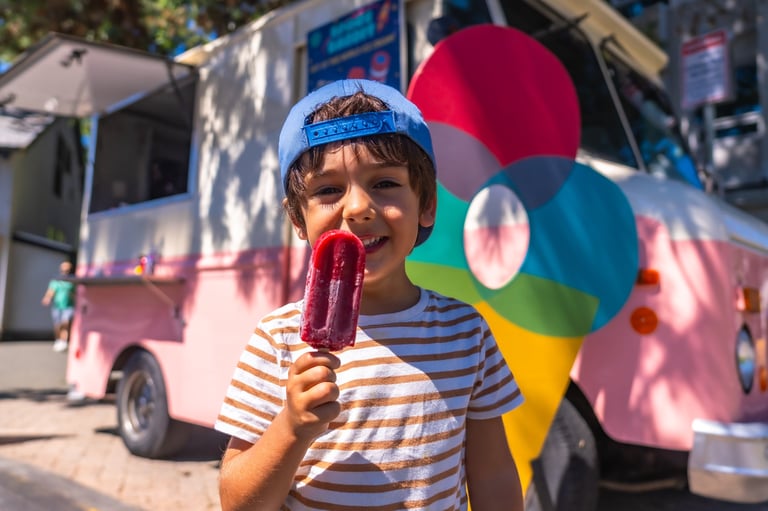 Happy child is eating a popsicle in front of a colorful food truck enjoying a sweet treat on a sunny day
