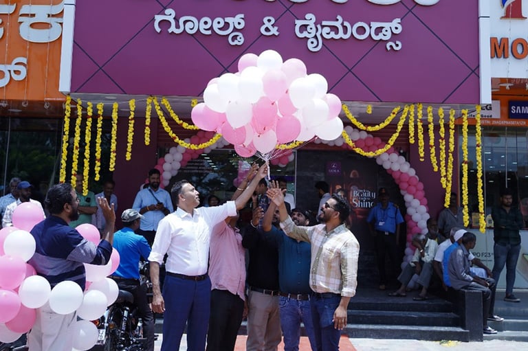 People holding pink and white balloons at a storefront decorated with gold garland and Kannada text signage