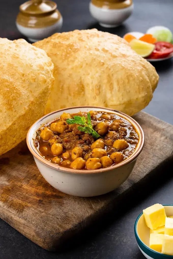 Bowl of chickpea curry with flatbread, fresh vegetables, and butter on a wooden board
