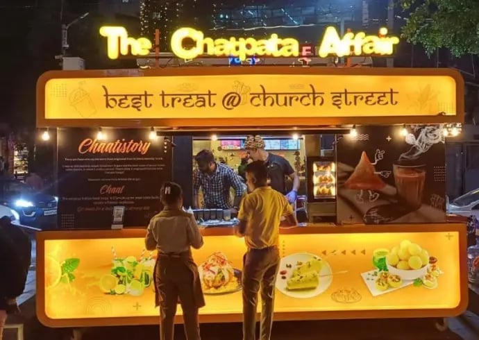 Illuminated late-night food cart called The Chapaata Affair with glowing yellow signage and menu display, two customers ordering at window