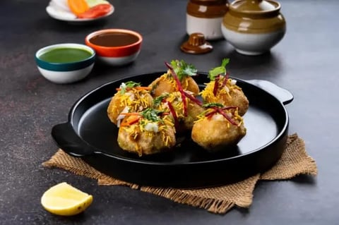 Golden fried shrimp appetizers on a black plate with sauce bowls and lemon wedge on dark table