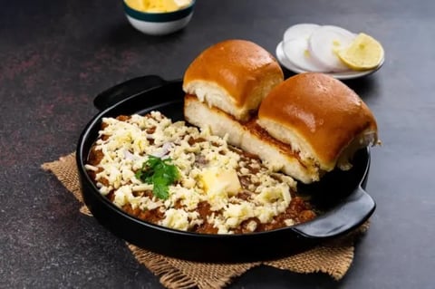 Black cast iron skillet with potato salad, two bread rolls, and sliced lemon on a dark surface with burlap placemat