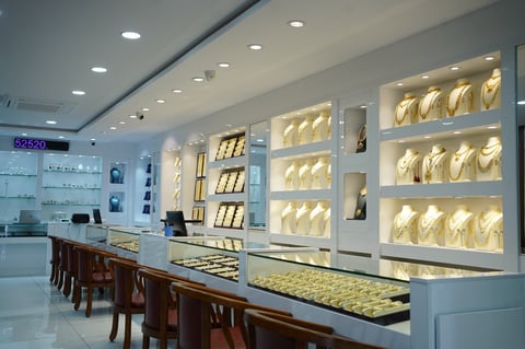 Luxury jewelry store interior with illuminated display cases, wooden seating, and gold-toned merchandise showcases under bright ceiling lights