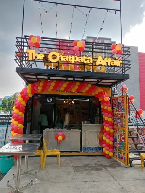 Colorful food vendor stall with yellow and red balloon decorations and signage on top
