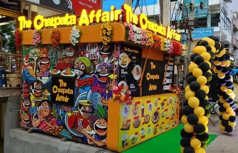 Colorful crepe food stand with yellow signage, decorated with vibrant artwork and yellow-black striped balloon columns at a street fair